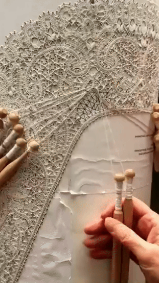 Hands working bobbin lace on a lace pillow with wooden bobbins and thread
