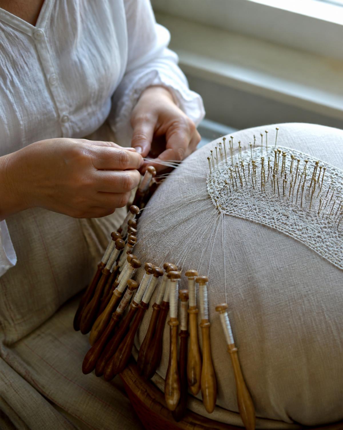 Video lesson still: hands crossing bobbins over a lace pillow